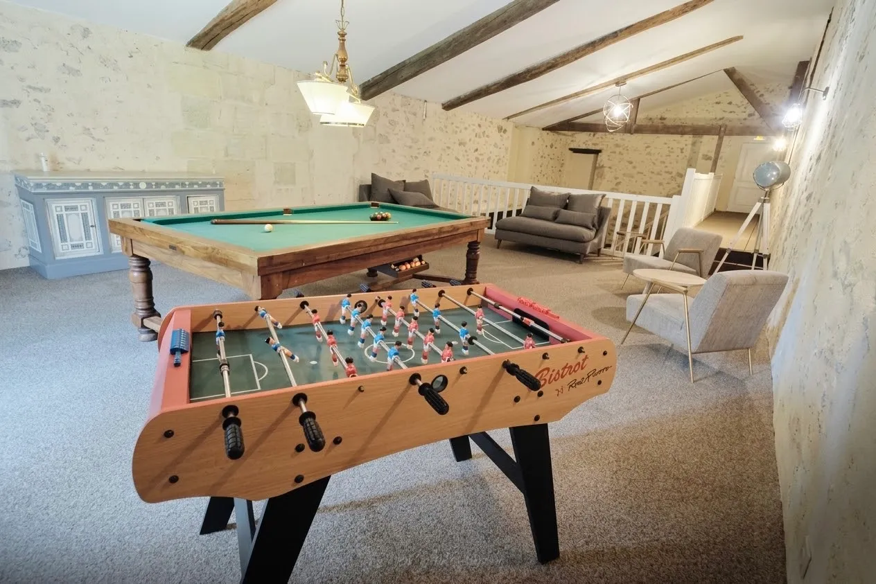 The games room at Château Meyre with table football, a billiard table and armchairs under exposed beams.