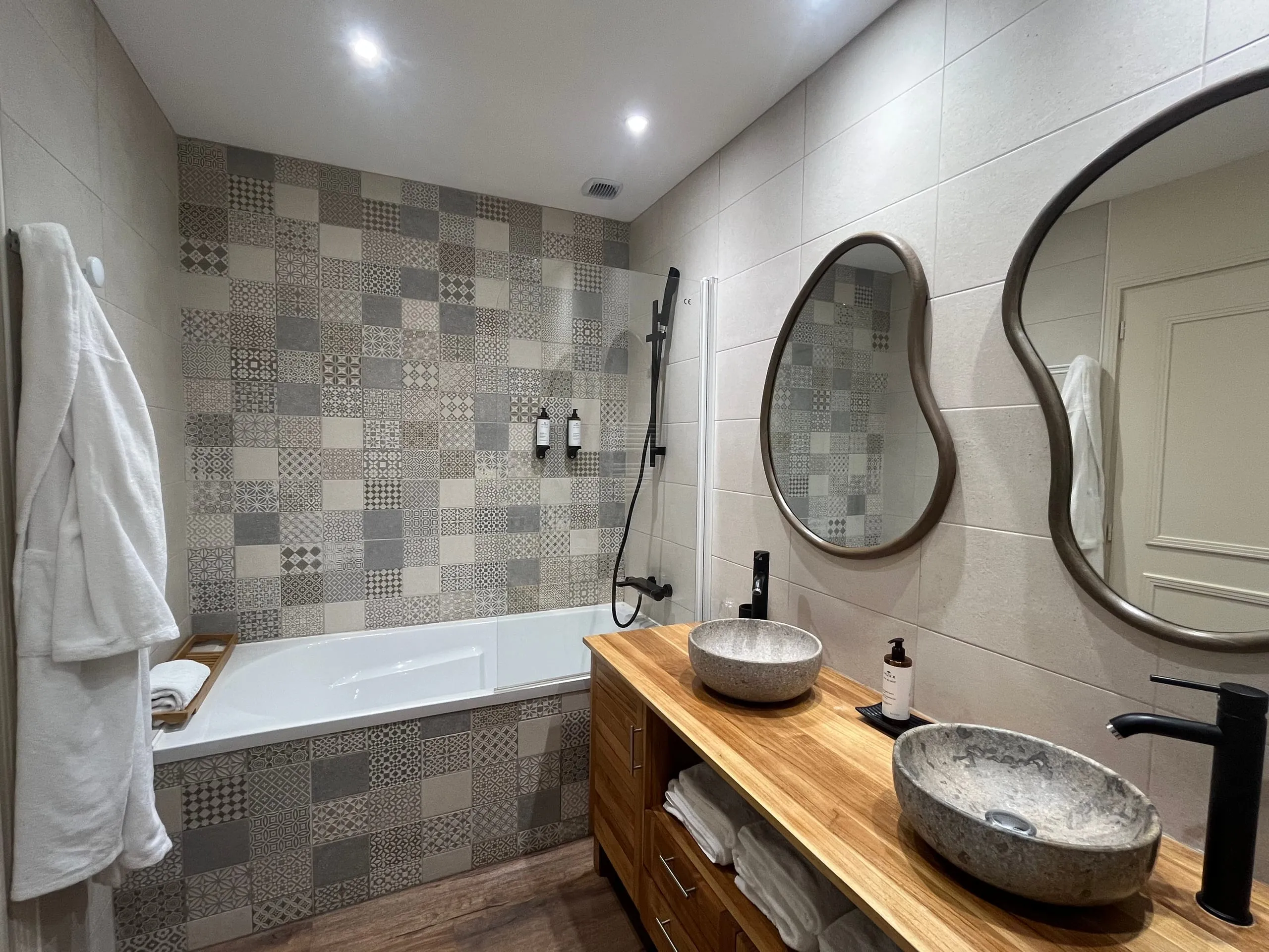Bathroom of the Cybele room with a bath, two stone basins and patterned tiles.