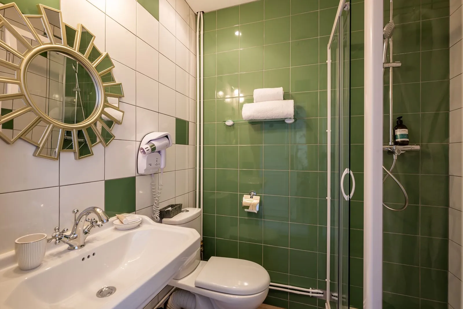 Salle de bain de la chambre Floralia avec douche vitrée, carrelage vert et miroir doré.