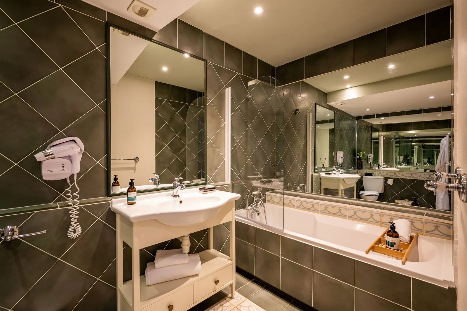Salle de bain de la chambre Gaïa avec baignoire, vasque blanche et carrelage sombre à motifs géométriques.