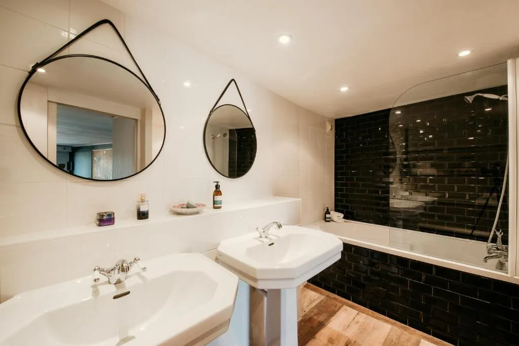 Salle de bain de la chambre Maïa avec deux vasques blanches et baignoire habillée de carrelage noir.