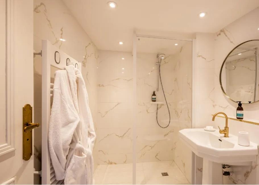 Salle de bain de la suite Matraé avec douche vitrée, vasque blanche et robinetterie dorée.