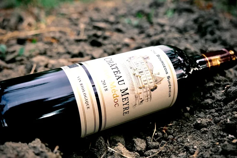 Bouteille de Château Meyre 2018 Haut-Médoc posée sur le sol du vignoble.