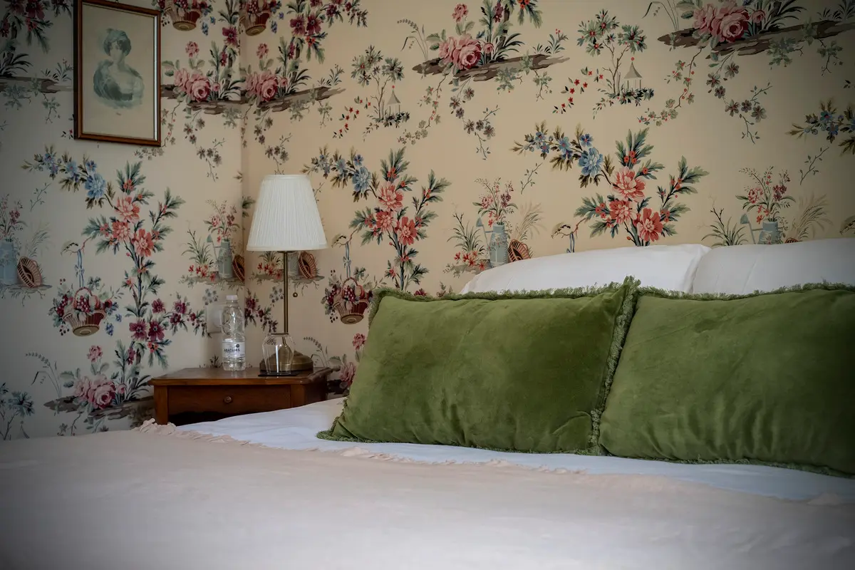Coussins en velours vert et papier peint fleuri dans la chambre Floralia du Clos de Meyre.