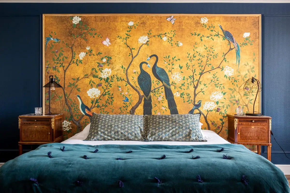 Lit double de la chambre Maïa devant un panneau doré décoré d’oiseaux et de fleurs au Clos de Meyre.