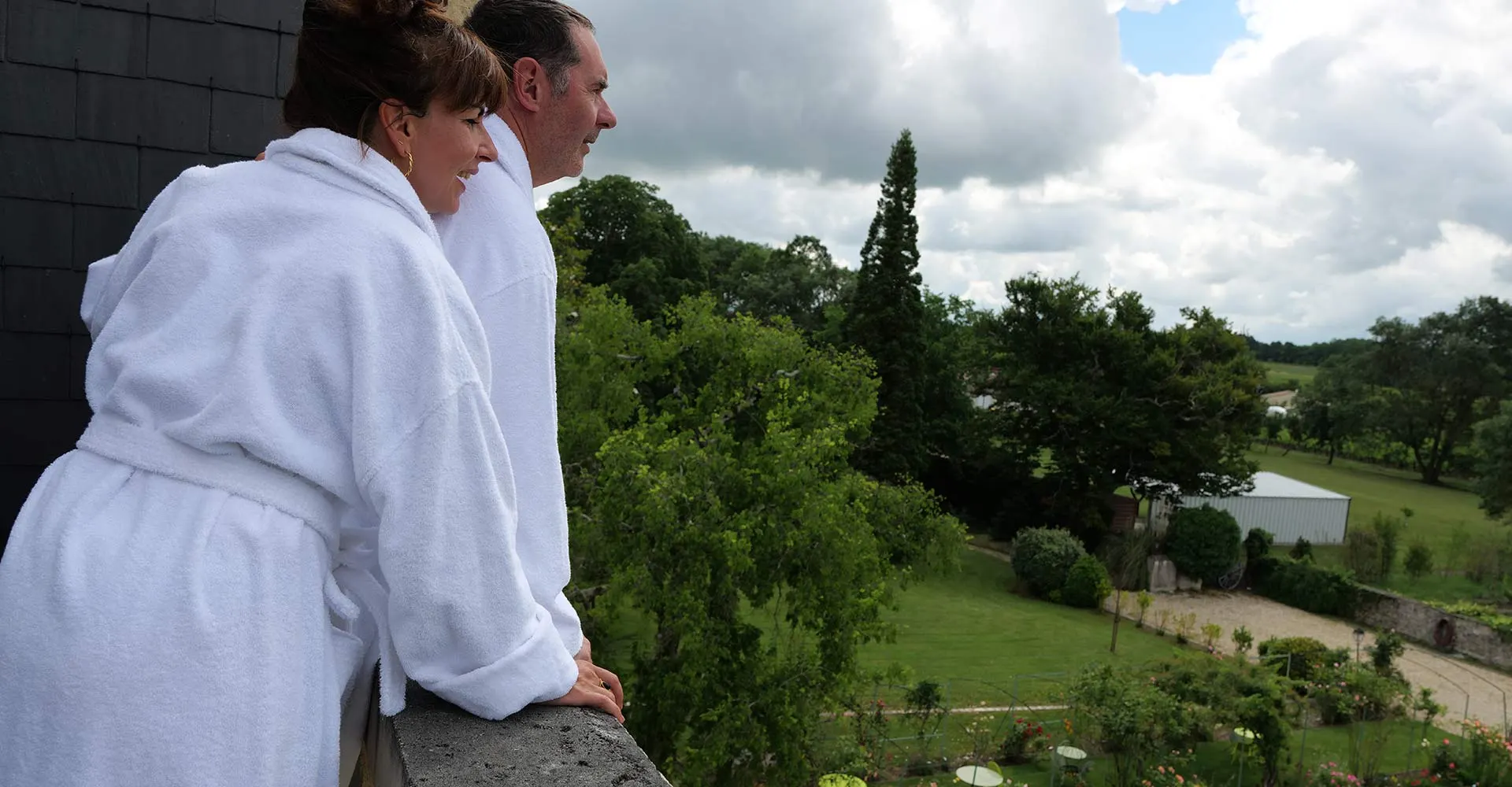Couple en peignoirs blancs sur un balcon face au parc du Clos de Meyre à Avensan.