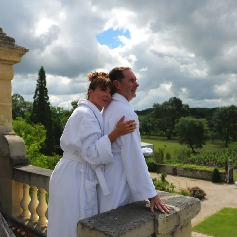 Couple in white bathrobes on a terrace facing the park at Clos de Meyre.