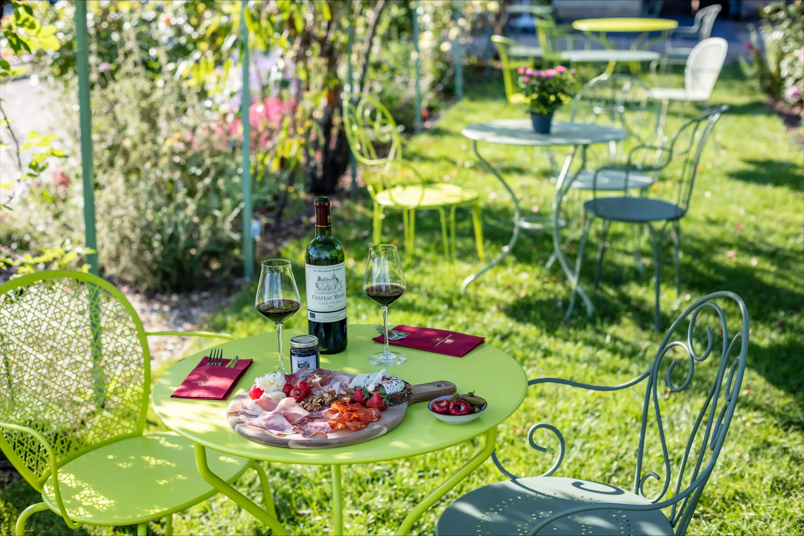 A platter of charcuterie and cheese with two glasses and a bottle of wine in the garden.